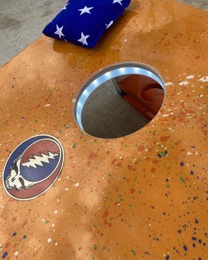 Outdoor games for family gatherings featuring a colorful bean bag toss board with a hole and decorative design.
