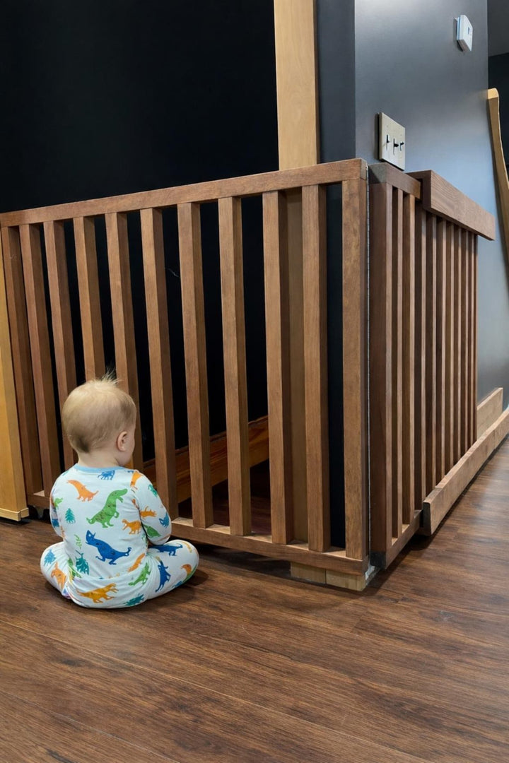 A baby sitting next to a retractable wall mounted baby gate, designed for safety and space efficiency.