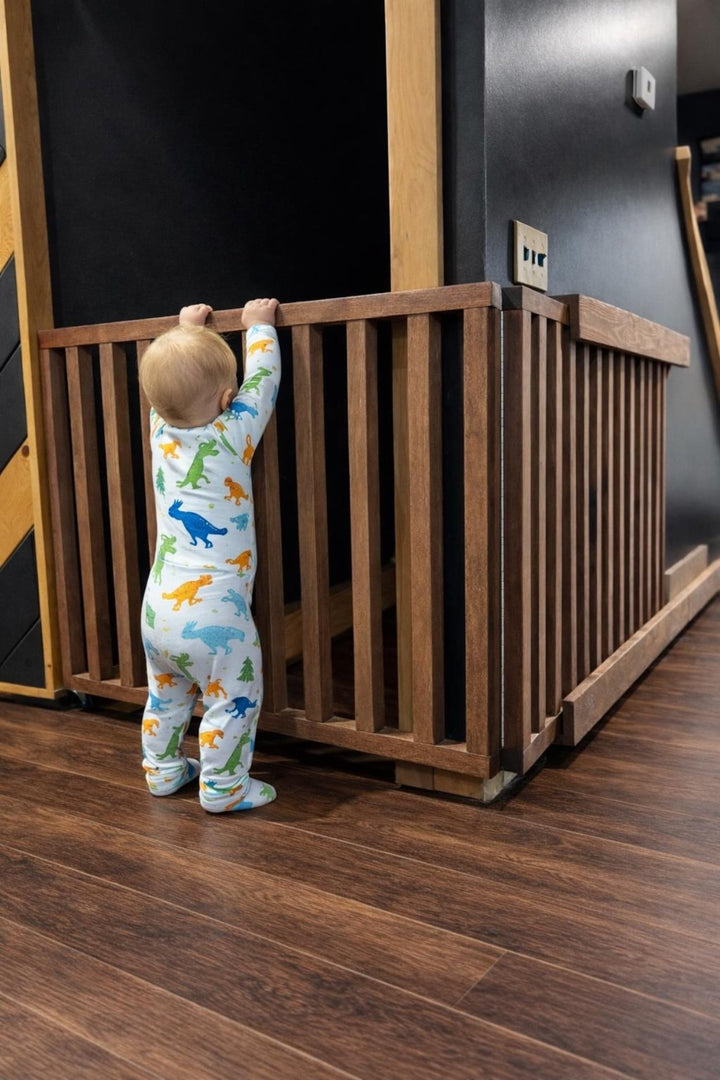Toddler reaching for a retractable wall mounted baby gate in a stylish interior.