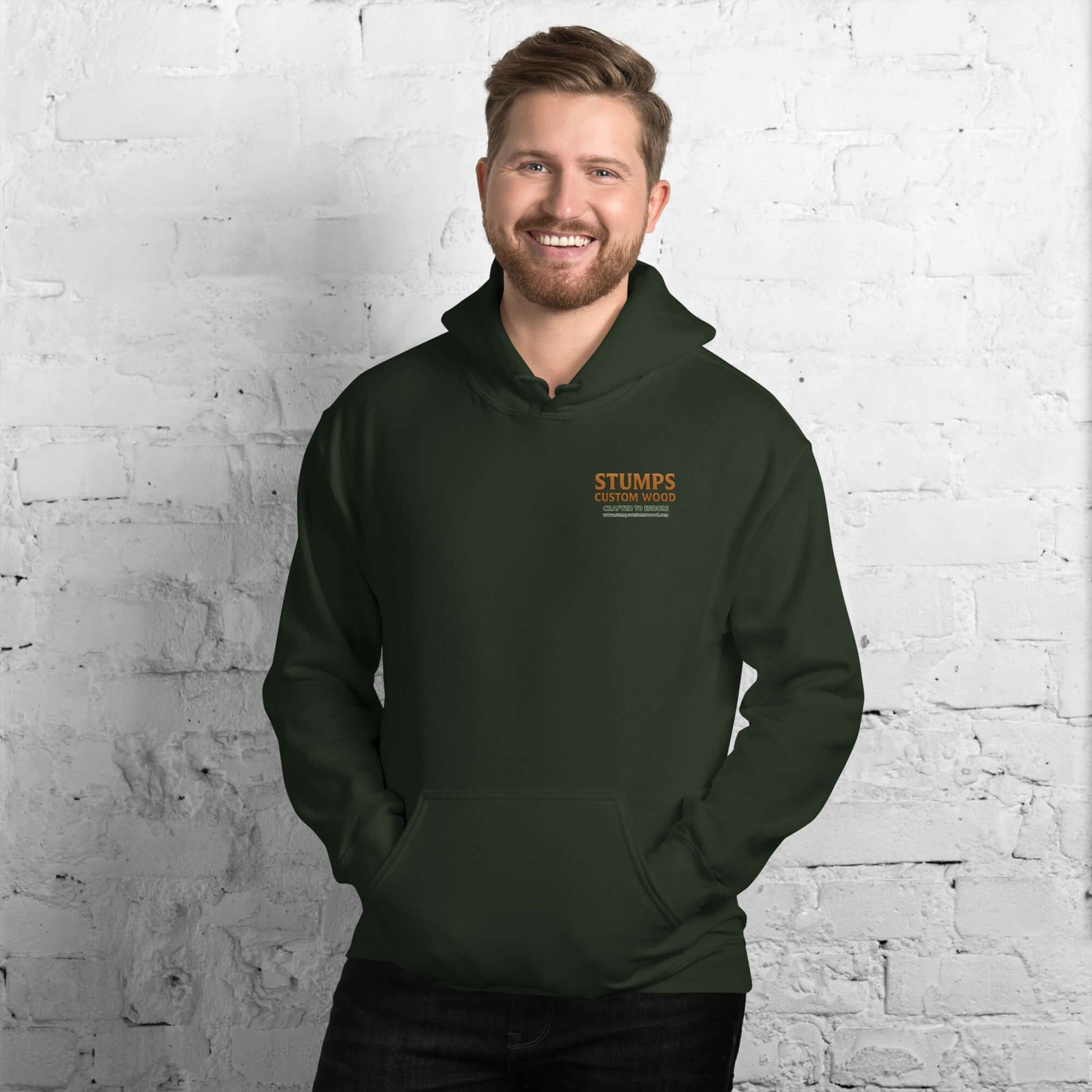 Stumps Custom Wood Unisex Hoodie in green worn by a smiling man against a brick wall background.