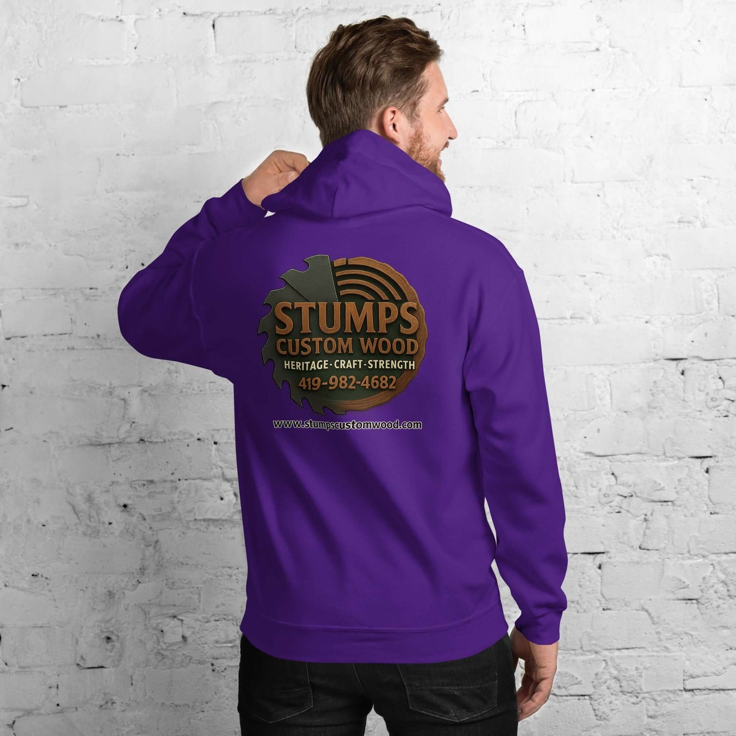 Stumps Custom Wood Unisex Hoodie in purple featuring logo on back laid against a textured white wall.